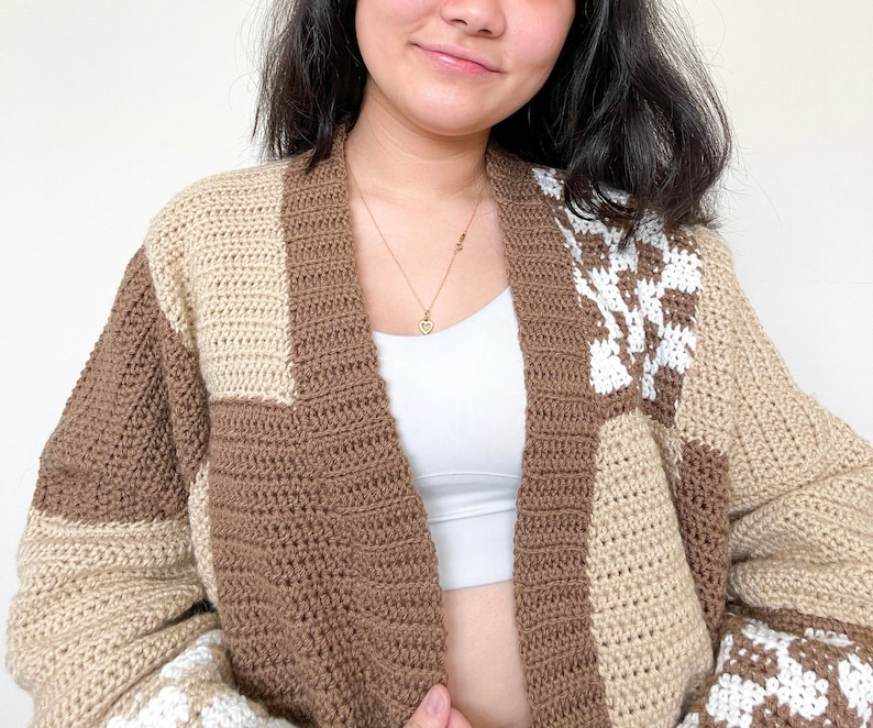May include: A brown and beige crocheted cardigan with a white and brown geometric pattern. The cardigan has a V-neck and long sleeves.