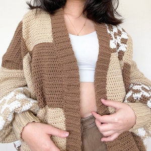 May include: A brown and cream crocheted cardigan with a patchwork design. The cardigan has a long, open front and long sleeves.