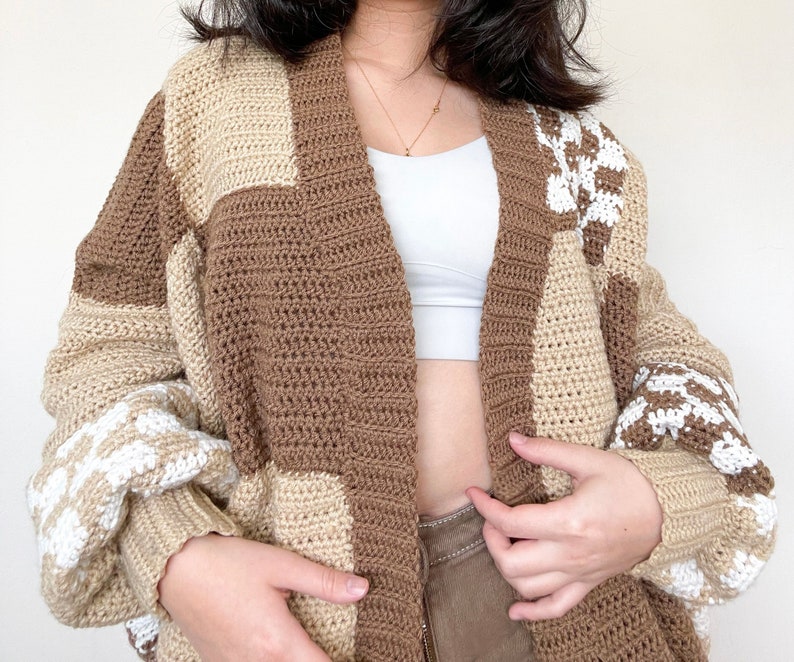 May include: A brown and cream crocheted cardigan with a patchwork design. The cardigan has a long, open front and long sleeves.