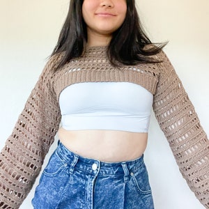 May include: A brown crocheted crop top with long sleeves. The top is made with a loose, open stitch pattern.