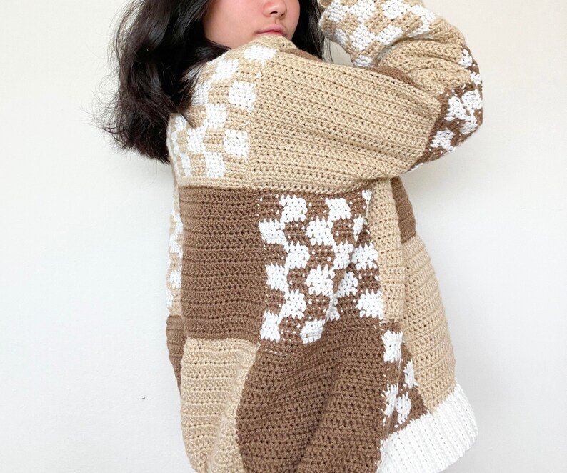 May include: A brown and white crocheted sweater with a patchwork design. The sweater has a loose fit and a long sleeve.