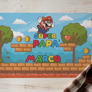 Puede incluir: Ilustración colorida con un personaje de dibujos animados con gorro rojo y peto azul saltando en una escena de videojuego. El texto dice "SUPER PAPA MARCO" en colores vibrantes, con monedas y árboles en el fondo. La imagen tiene un cielo azul y plataformas de ladrillo.