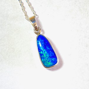 May include: A silver chain necklace with a teardrop-shaped pendant featuring a blue opal gemstone with green and blue flashes.