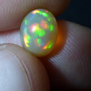 May include: A white oval opal gemstone with green, red, and orange flashes of colour.