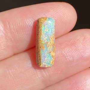 May include: A light blue and white opal cabochon with a brown matrix. The opal is rectangular in shape and has a smooth, polished surface.