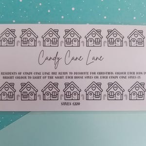 Könnte beinhalten: Eine weiße Karte mit schwarzen Strichzeichnungen von Häusern und Zuckerstangen. Der Text "Candy Cane Lane" ist kursiv geschrieben. Der Text der Karte ermutigt zum Ausmalen der Symbole für Weihnachten. Die Karte spart £220.