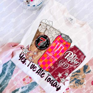 Könnte beinhalten: Weißes T-Shirt mit einem Grafikdesign, das eine Kaffeetasse, eine orangefarbene und pinkfarbene Monster-Energydrink-Dose und eine Dr. Pepper-Dose zeigt. Der Text "Yes, I've Ate Today" ist ebenfalls auf dem Shirt aufgedruckt.