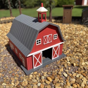 May include: A miniature red barn model with a gray roof, white trim, and a white cupola. The structure features a large open front doorway with white cross-braced doors, smaller side doors, and windows with white frames on the front facade.