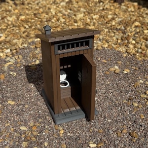May include: A miniature brown outhouse model featuring vertical siding, a slanted roof with a small chimney, and an open door revealing a white toilet seat inside. The structure is built on a dark gray base and includes a rectangular vent.