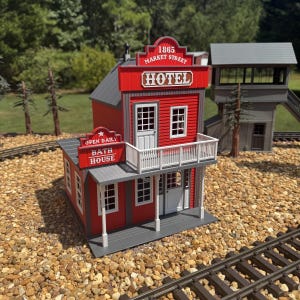 May include: A miniature model of a red and gray two-story hotel and bath house building. The facade features white text reading 1865 MARKET STREET HOTEL and OPEN DAILY BATH HOUSE. The structure includes a white balcony, windows, and doors.