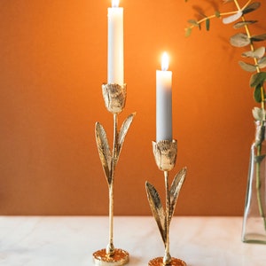 Puede incluir: Dos candelabros de oro con forma de tulipán con velas blancas encendidas en su interior.