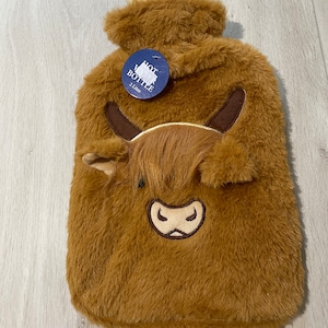 May include: Brown fluffy hot water bottle with a Highland Cow face on the front. The bottle has a blue tag that says "Hot Water Bottle 2 Litre".
