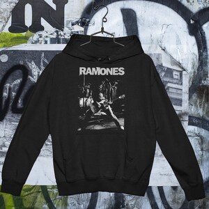 May include: Black hooded sweatshirt with a white graphic print of the band "Ramones" performing on stage.