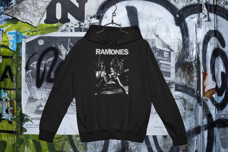 May include: Black hooded sweatshirt with a white graphic print of the band "Ramones" performing on stage.