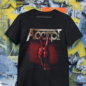 Pode incluir: Camiseta preta com um logotipo dourado "ACCEPT" e uma mão ensanguentada fazendo um sinal de paz. O texto "Blood of the Nations" está impresso abaixo do logotipo.