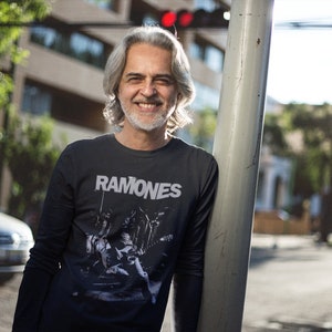 May include: A man wearing a black long-sleeved shirt with a white graphic print of a band called "Ramones".
