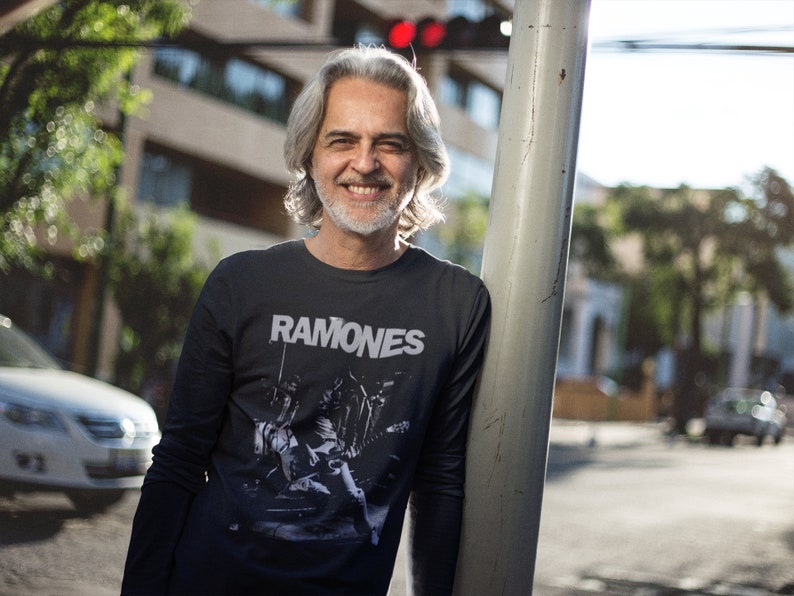 May include: A man wearing a black long-sleeved shirt with a white graphic print of a band called "Ramones".