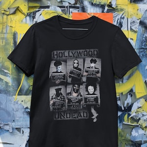 May include: Black t-shirt with a graphic print of a band called "Hollywood Undead". The graphic features six mugshots of band members with the text "Hollywood Police Department" and arrest dates.