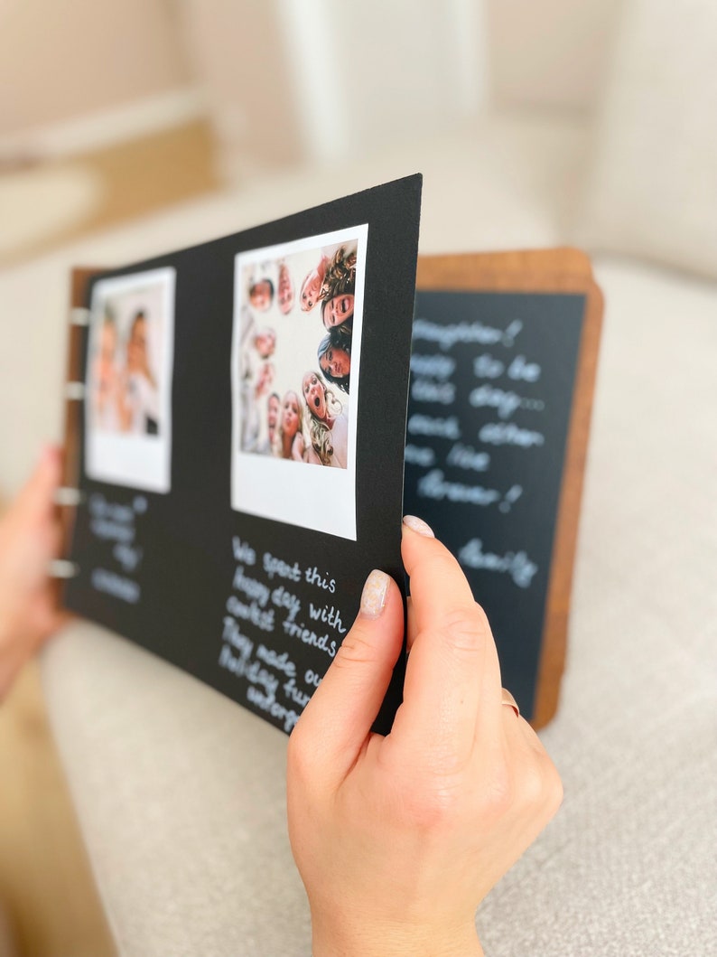 May include: A photo album with a wooden cover and black pages. The album is open, revealing two photos and handwritten text. The photos are of people. The text on the page reads "We spent this happy day with closest friends. They made our holiday fun, unforgettable."