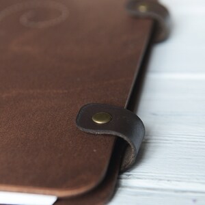 May include: A brown leather journal with a flap closure and a brass button. The journal has a worn, vintage look.