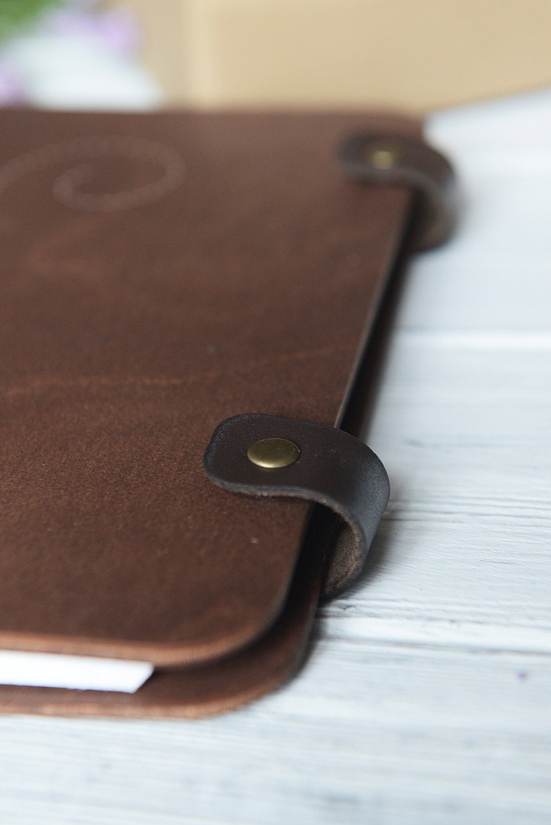 May include: A brown leather journal with a flap closure and a brass button. The journal has a worn, vintage look.