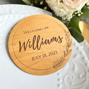 May include: A round wooden sign with the text "Wedding by Williams July 18, 2023" and a floral design.