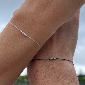 May include: Two simple bracelets, one white with white beads and one black with grey beads.