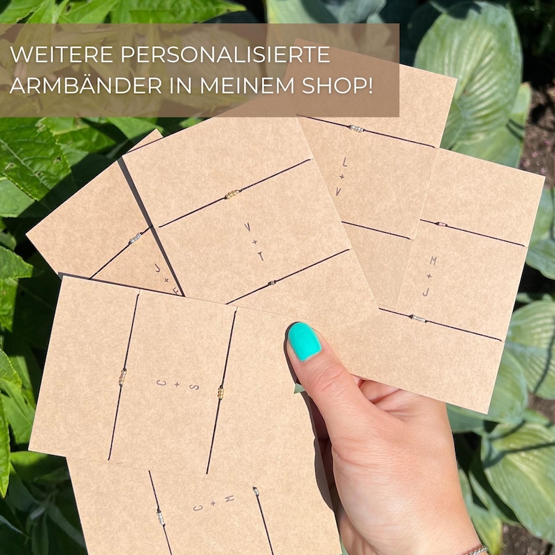May include: A hand holding several personalised bracelets on brown cards. Each card has a black string bracelet with a small decorative bead. The cards have initials and the text "WEITERE PERSONALISIERTE ARMB&Auml;NDER IN MEINEM SHOP!"