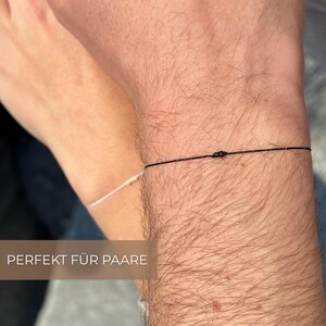 May include: Close-up of two wrists, each with a delicate string bracelet. One bracelet is black, the other white. The image has the text "PERFEKT F&Uuml;R PAARE".