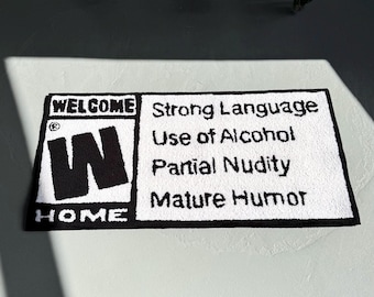 Puede incluir: Una alfombra rectangular blanca con texto negro y un logotipo negro. El texto dice "WELCOME HOME" y enumera advertencias de contenido: "Strong Language, Use of Alcohol, Partial Nudity, Mature Humor".