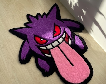 Puede incluir: Alfombra de dibujos animados de color morado y rosa con un fantasma con una lengua grande que sobresale. El fantasma tiene ojos rojos y una boca blanca.