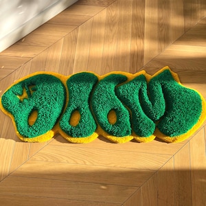Op de afbeelding: Een groen en geel vloerkleed met het woord "DOWN" gespeld in grote, bolle letters.