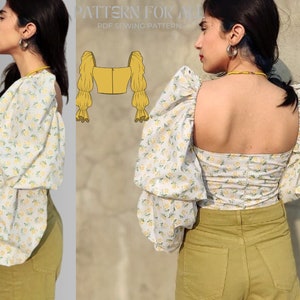 May include: A white top with a floral print and large puffed sleeves. The top has a square neckline and a fitted bodice. The model is wearing the top with high-waisted pants.
