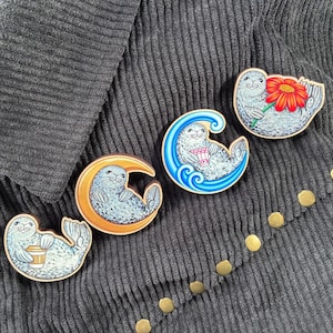 May include: Four wooden pins featuring spotted seals. One seal holds a coffee cup, one rests on a yellow crescent moon, one sits inside a blue wave holding a patterned cup, and one holds a large red flower with a yellow centre.