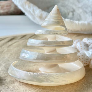 May include: A white seashell sculpture shaped like a spiral tree. The shell is iridescent and has a smooth, polished finish.
