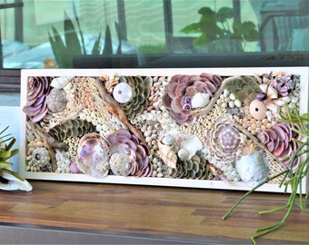 May include: A framed wall art piece made of various seashells, including sand dollars, clams, and other shells in shades of pink, white, and brown. The shells are arranged in a mosaic pattern, creating a textured and organic look.