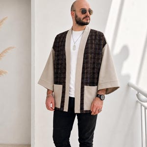 May include: A brown and beige kimono-style jacket with a plaid pattern on the front and sleeves. The jacket has two front pockets and is worn over a white shirt and black pants. The jacket is a stylish outerwear option.