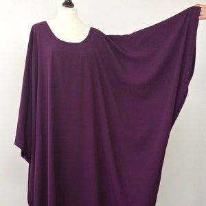 May include: A long, loose-fitting, purple,  tunic-style top with a round neckline. The top has wide, flowing sleeves.