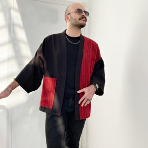 May include: A black and red striped kimono with a pocket on the left side. The kimono is open in the front and has a black collar.