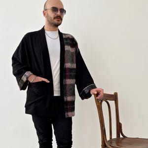 May include: A black and plaid kimono-style jacket with long sleeves and a pocket on the left side. The jacket is worn over a white t-shirt.