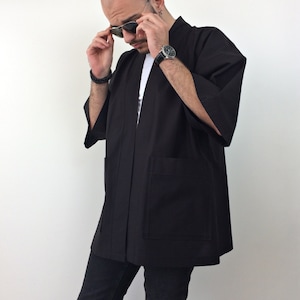 May include: A black kimono with long sleeves and two pockets. The kimono is open in the front and has a simple design.