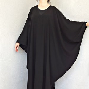 May include: A black, long-sleeved, loose-fitting dress with a v-neckline. The dress is made of a soft, flowing fabric and has a relaxed fit.