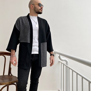 May include: A black and gray patterned kimono with a white t-shirt underneath. The kimono has a long sleeve and a relaxed fit.