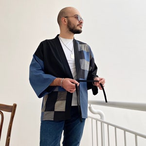 Könnte beinhalten: Ein blaues und schwarzes Patchwork-Kimono mit einem schwarzen Gürtel. Das Kimono wird über einem weißen T-Shirt und einer blauen Jeans getragen.