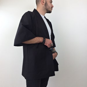 May include: A black kimono-style jacket with long sleeves and a single pocket on the left side. The jacket is open in the front and has a relaxed fit.