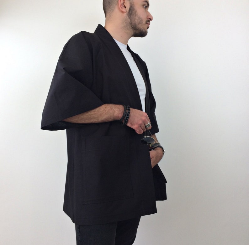 May include: A black kimono-style jacket with long sleeves and a single pocket on the left side. The jacket is open in the front and has a relaxed fit.