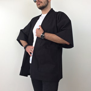 May include: A black kimono with long sleeves and a simple design. The kimono is open in the front and has a pocket on the left side.