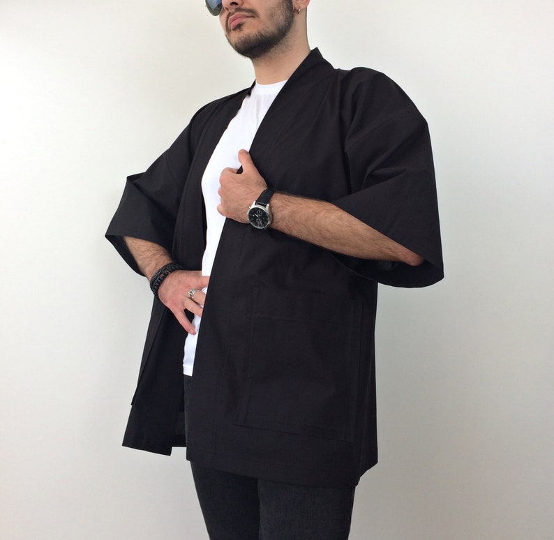 May include: A black kimono with long sleeves and a simple design. The kimono is open in the front and has a pocket on the left side.