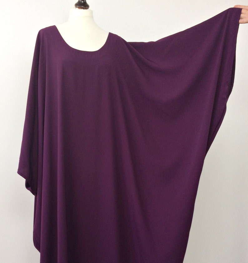 May include: A long, loose-fitting, purple,  tunic-style top with a round neckline. The top has wide, flowing sleeves.