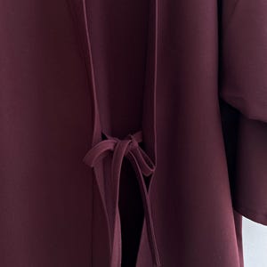 May include: A burgundy kimono with a long tie at the waist. The tie is tied in a bow at the front of the garment.